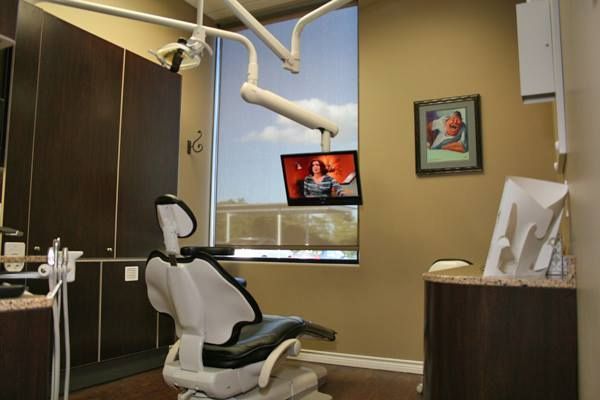 Dental exam room with chair, overhead light, TV, and window with a view.