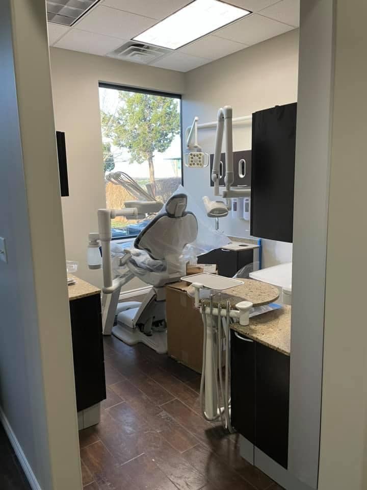Dental examination room, dental chair, and equipment. Dark wood floors, and cabinets with a window in the background.