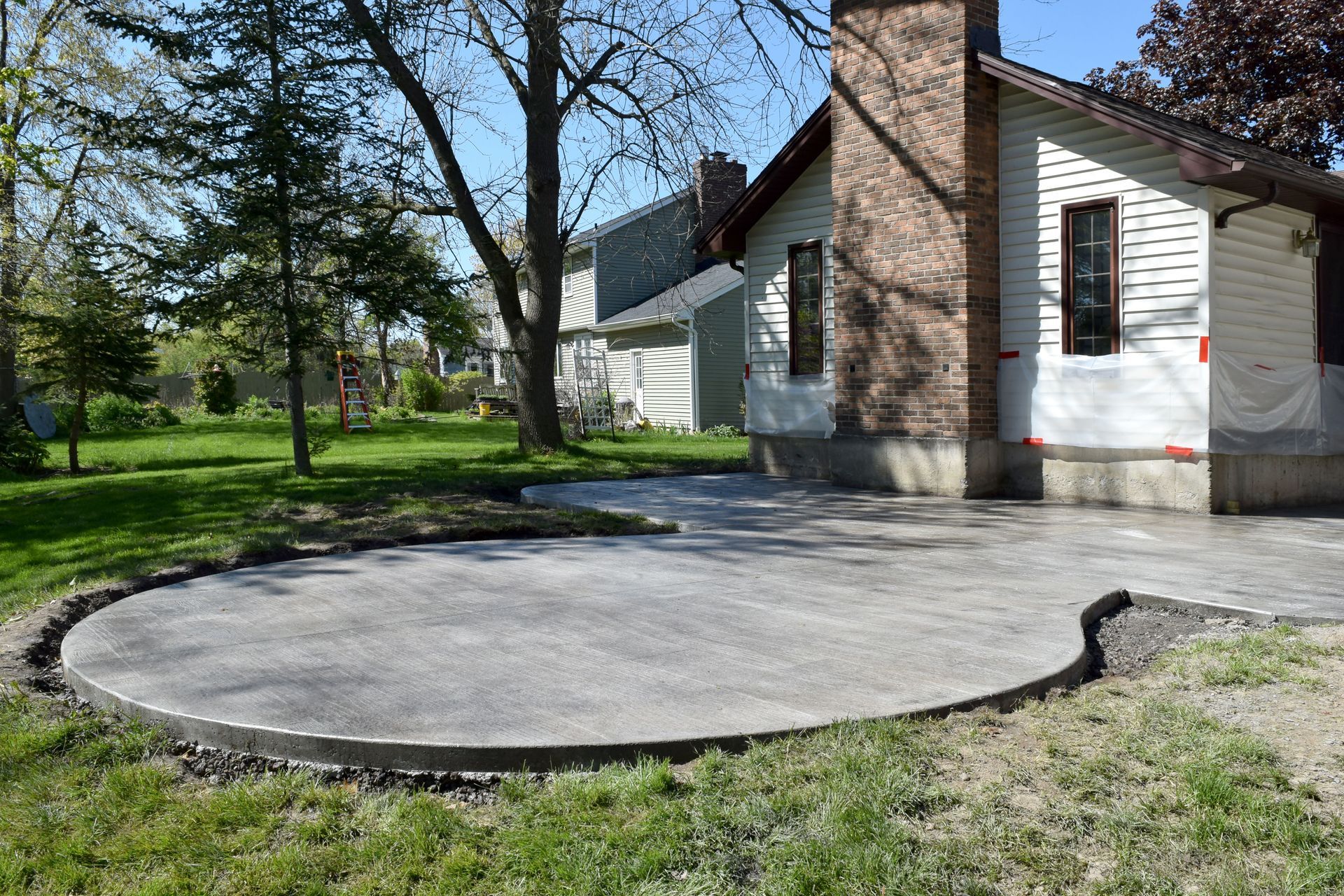 Concrete patio beside a brick-and-white house with trees and grass in the yard