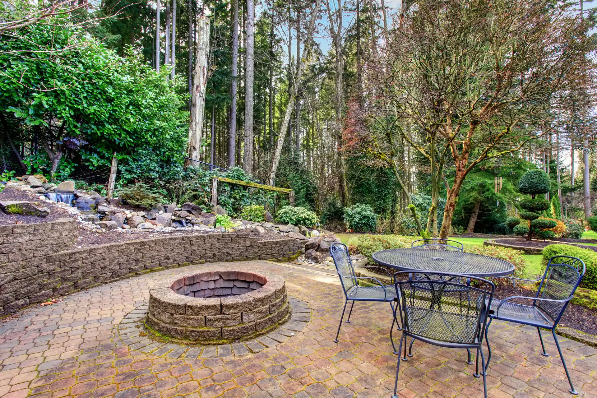 Patio with fire pit and metal table and chairs in a wooded backyard