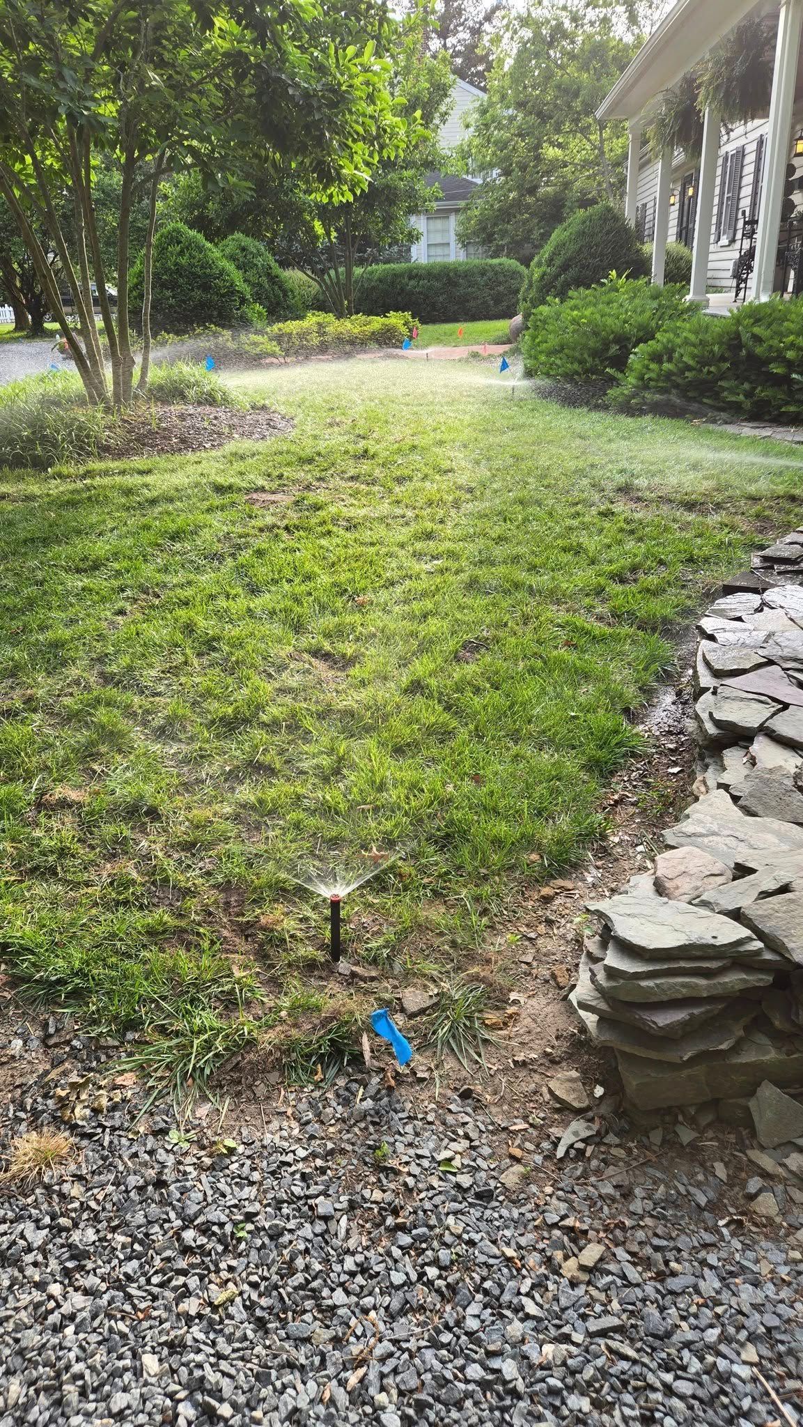 Gravel path beside a grassy yard and stone wall, with trees and a house in the background.