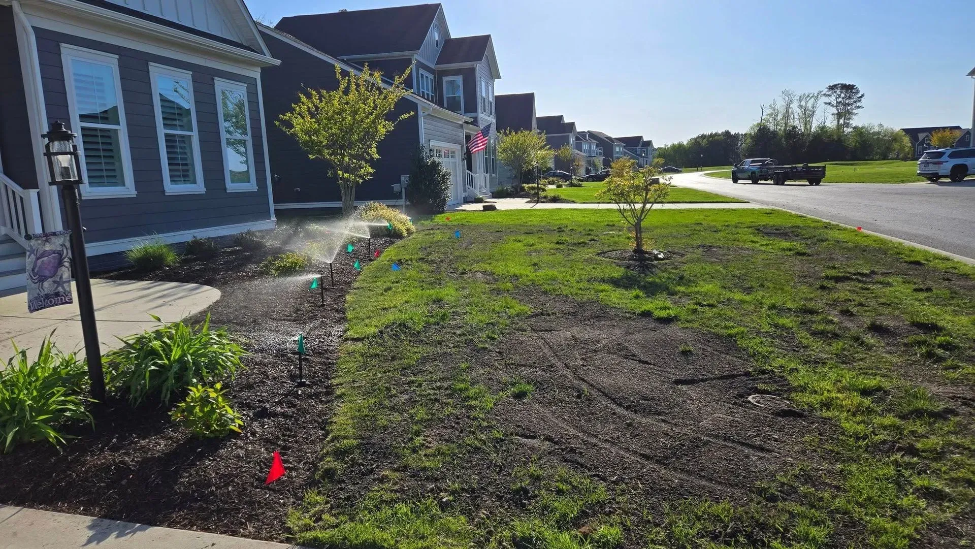 Suburban sidewalk and street with a newly landscaped grassy yard beside houses on a sunny day