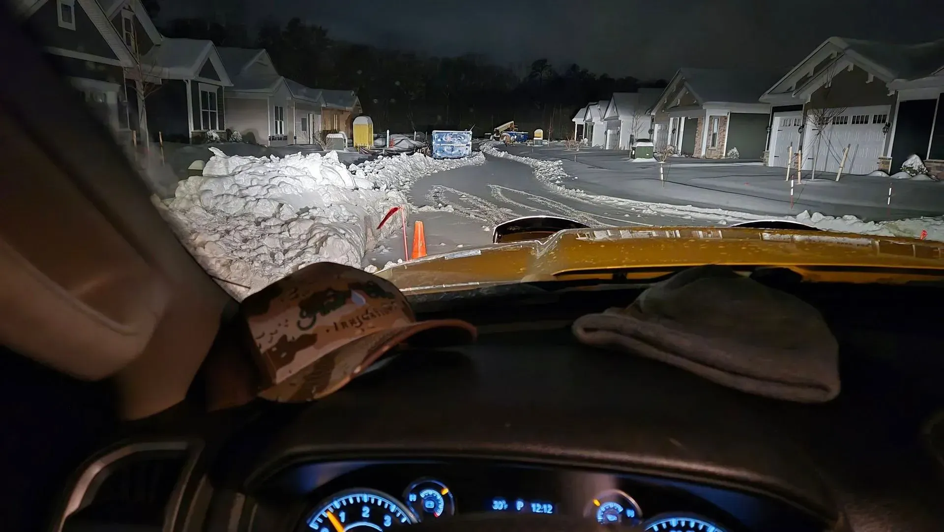 Driver’s view of a snowy residential street at night, with a car dashboard visible in the foreground.