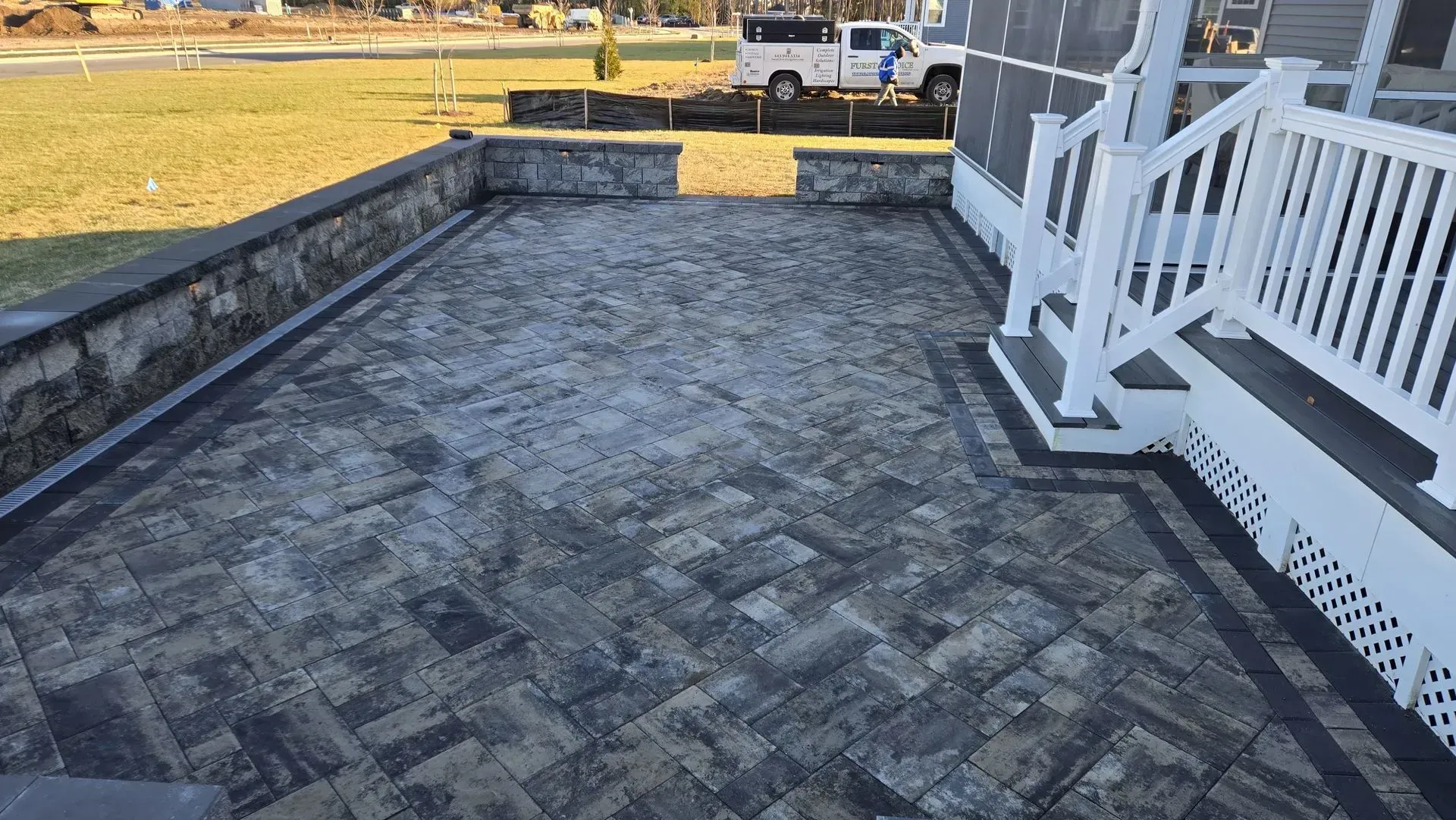 Stone patio beside white porch railing, with a parked truck and lawn in the background.