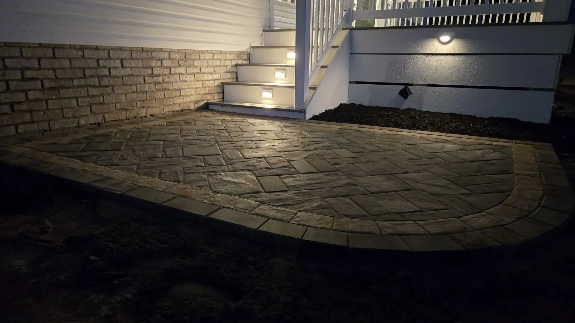 Stone walkway leading to a lit porch stairs beside a white house at night