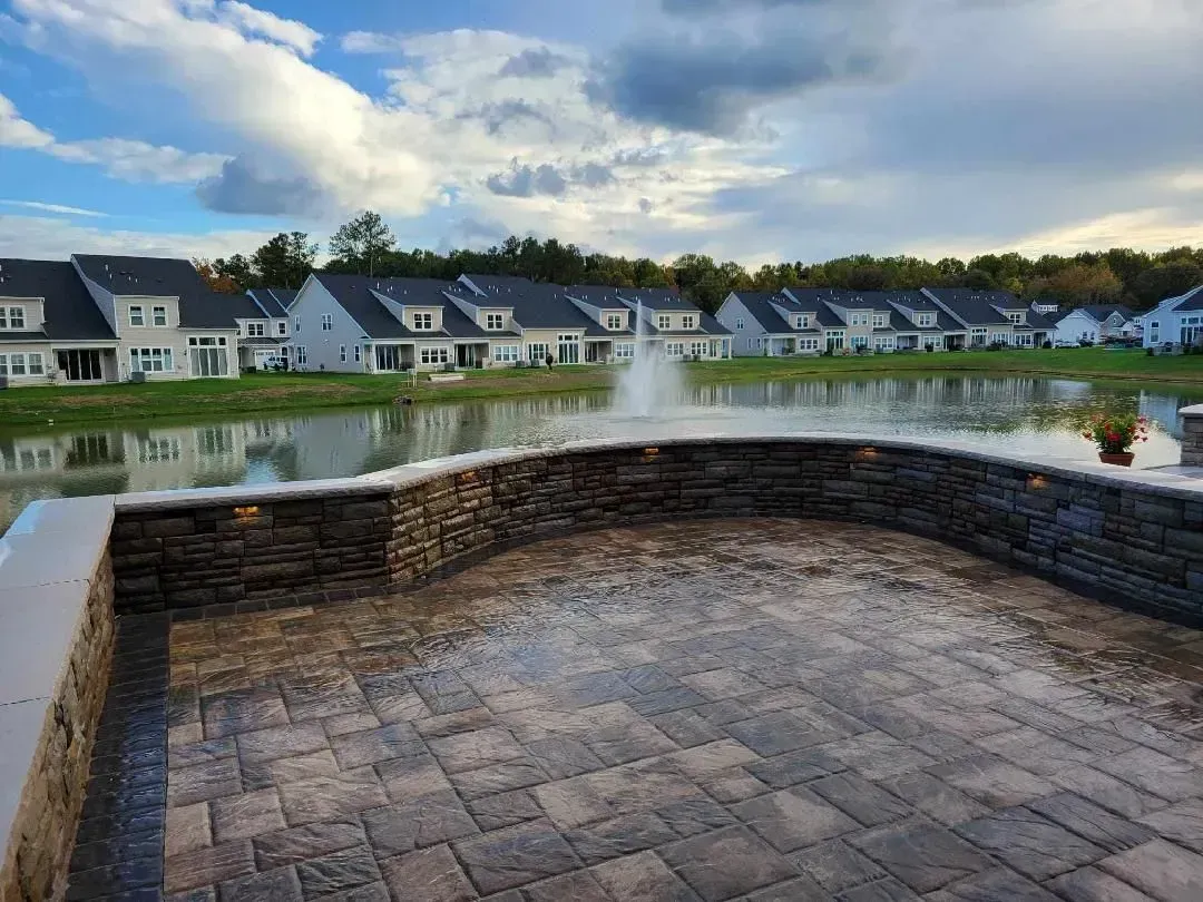 Stone patio overlooking a calm pond with row houses and cloudy sky beyond