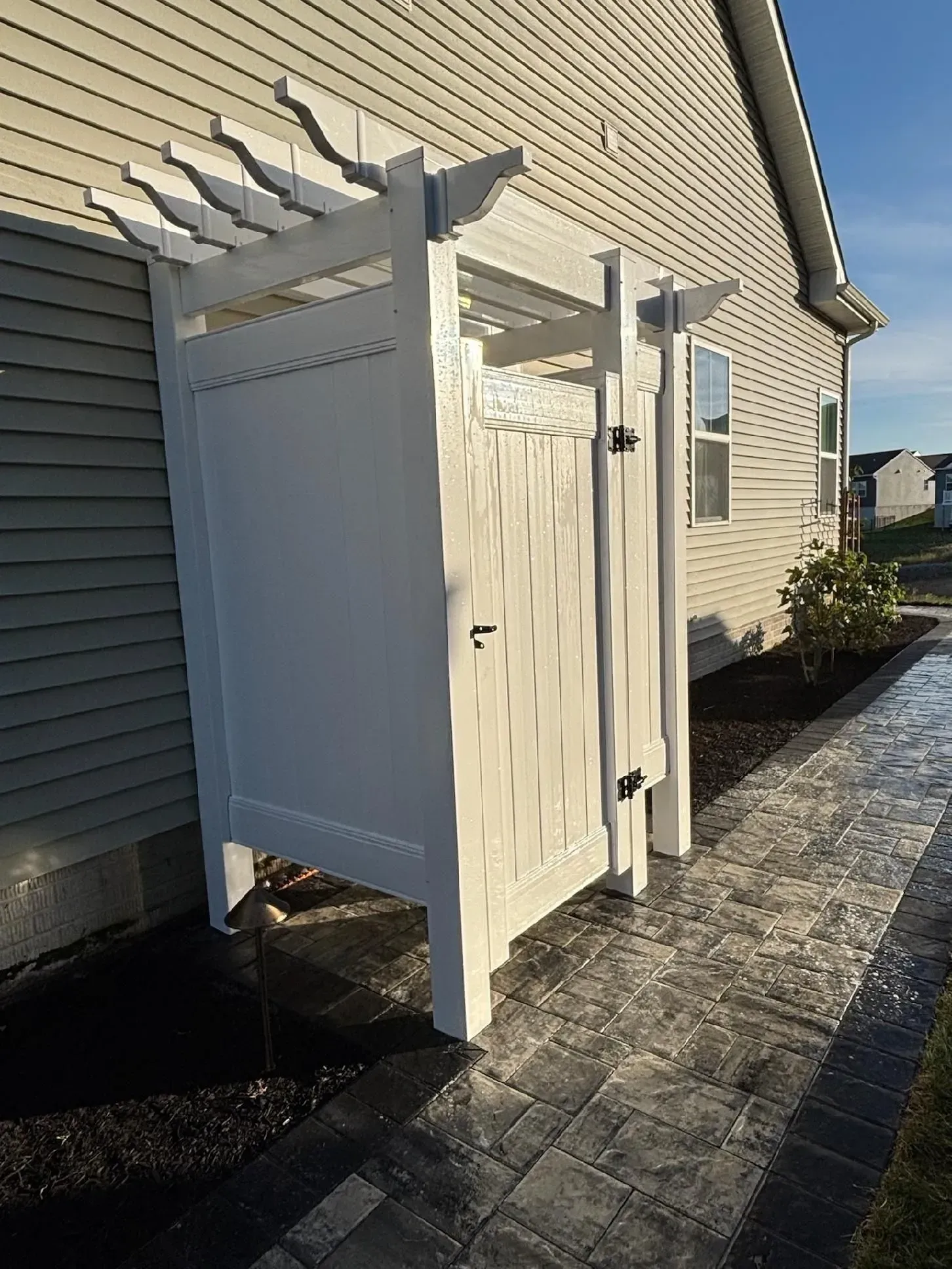 White privacy screen and pergola beside a beige house along a paved side yard.
