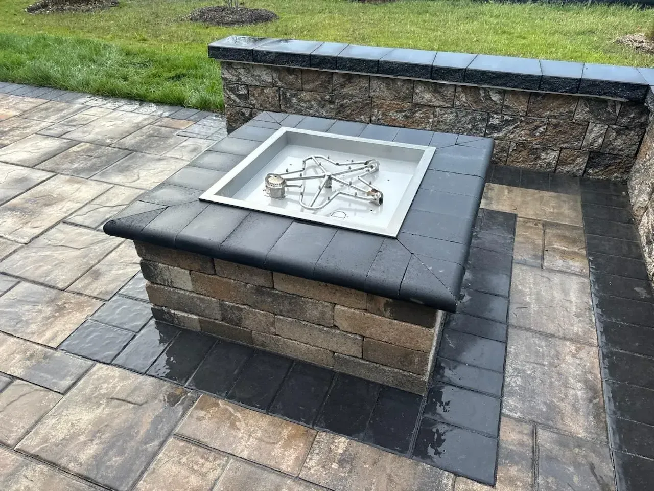 Outdoor stone fire pit with a metal insert on a paved patio beside a grass lawn