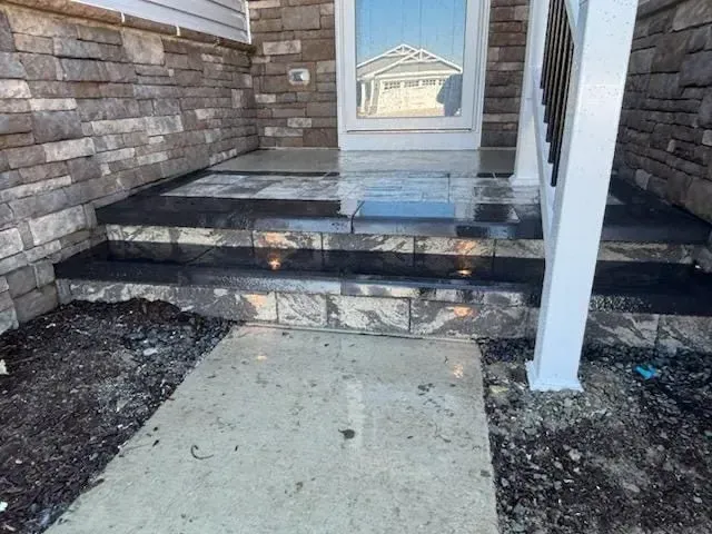 Front porch steps with stone siding, a white support post, and a concrete walkway leading to the entry door