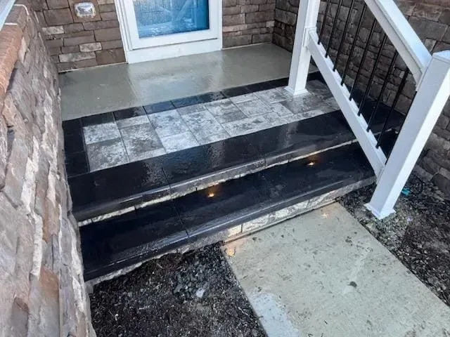 Front porch steps with black and gray stone, a white railing, and a blue door.