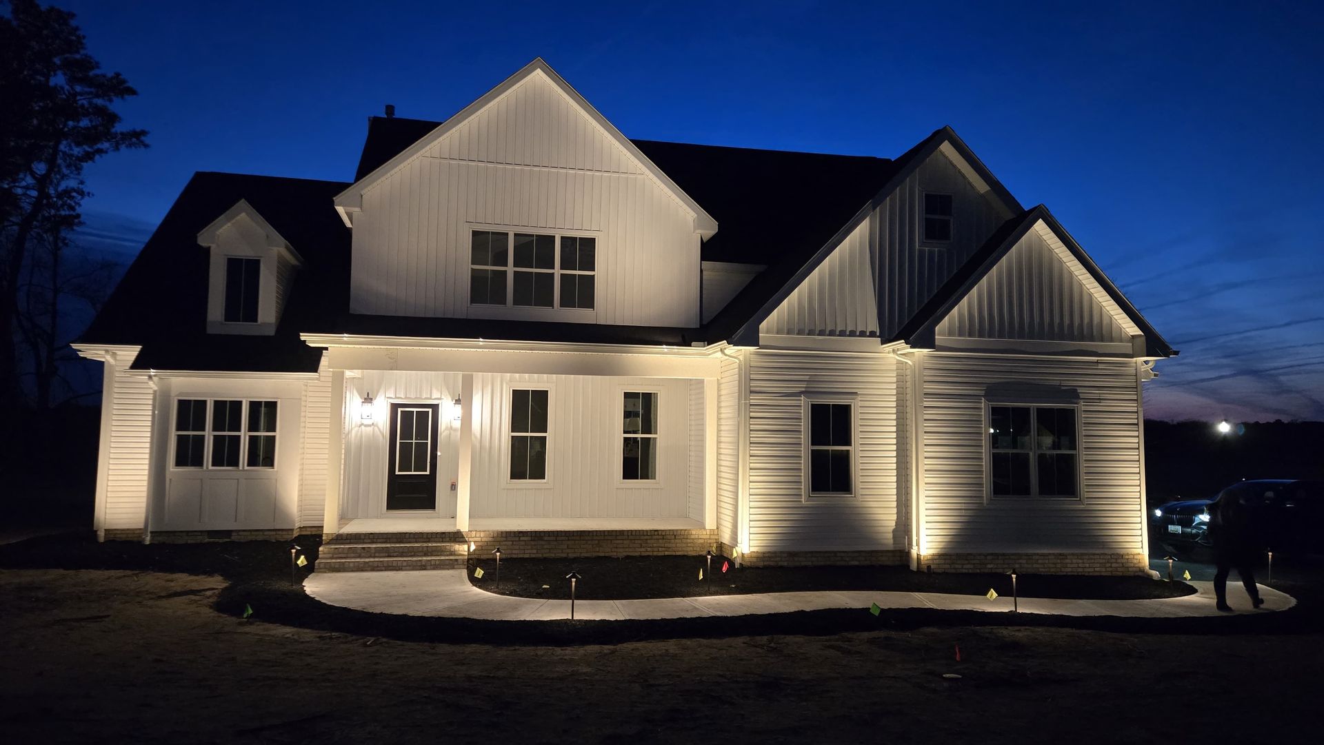 White house with lit exterior lights at dusk against a dark blue sky