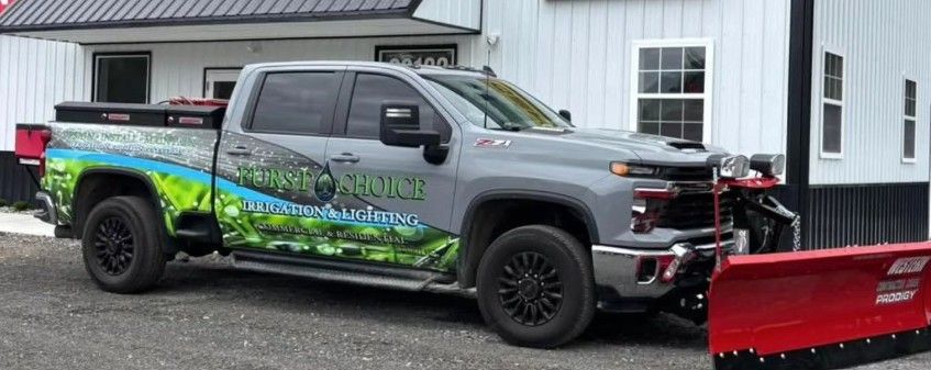 Gray pickup truck with green graphics and a red snowplow parked outside a building