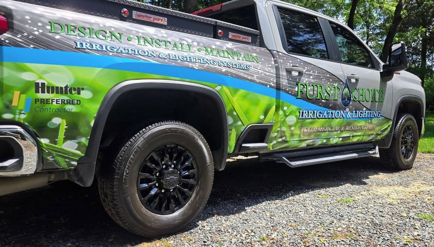 Green-and-silver lifted pickup truck with black rims and racing decals parked on gravel