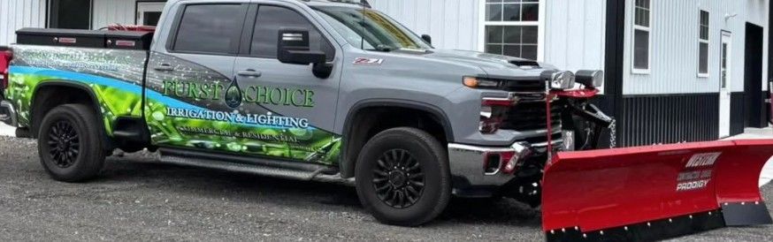 Gray pickup truck with green graphics attached to a red snow plow in front of a house