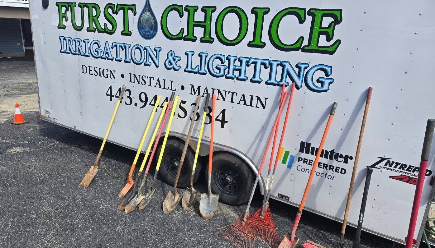 Utility trailer with “First Choice Electrical & Lighting” signage and tools leaning against it outdoors