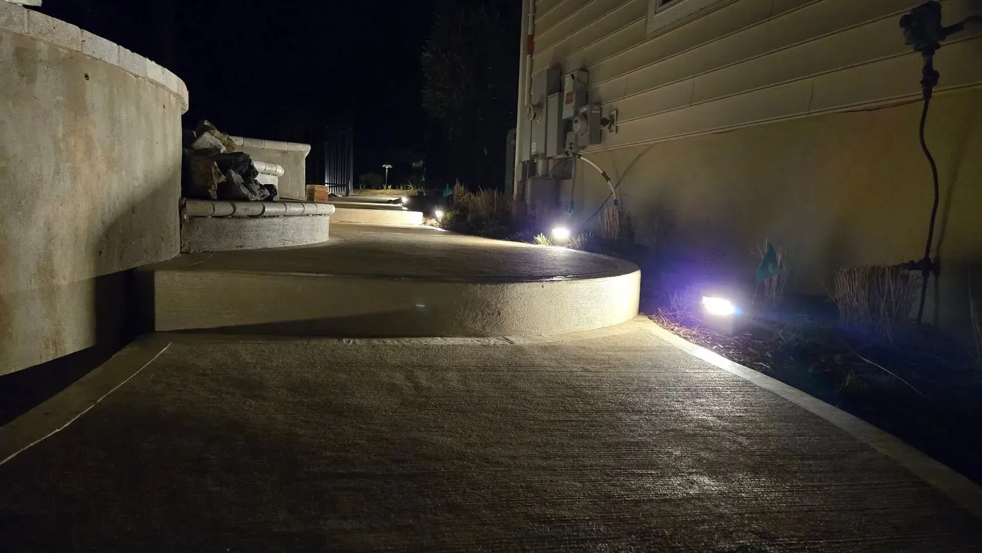 Nighttime walkway with curved concrete walls and several ground lights illuminating the path.
