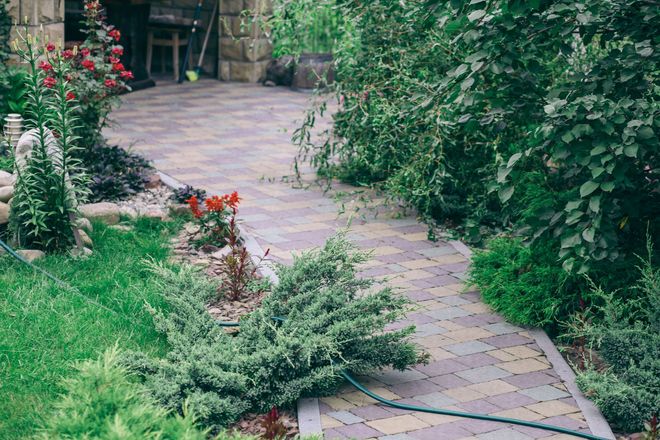 Curved stone garden path bordered by lush green shrubs and colorful flowers