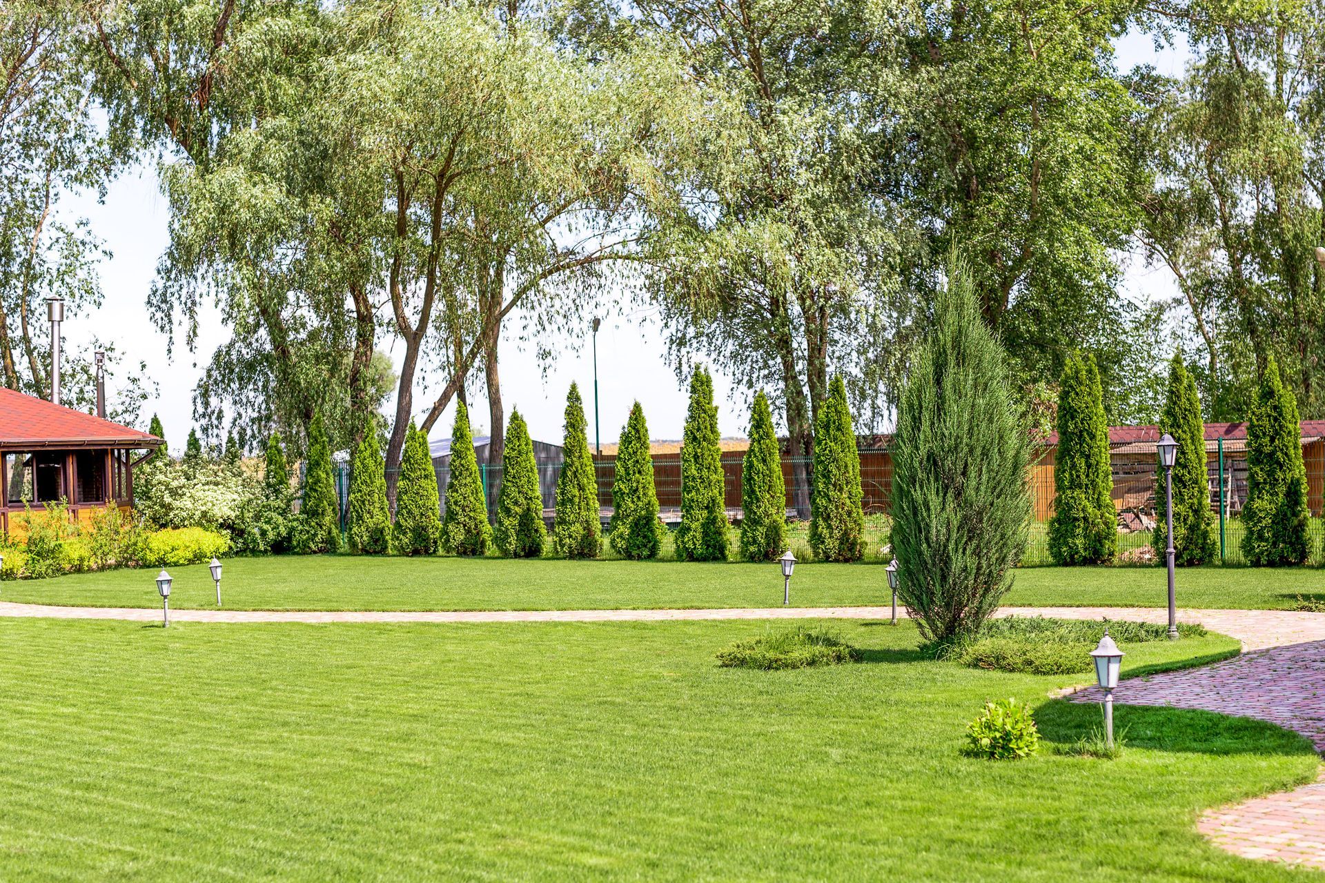 Lush green garden with trees, trimmed hedges, and a winding path beside a red-roofed building