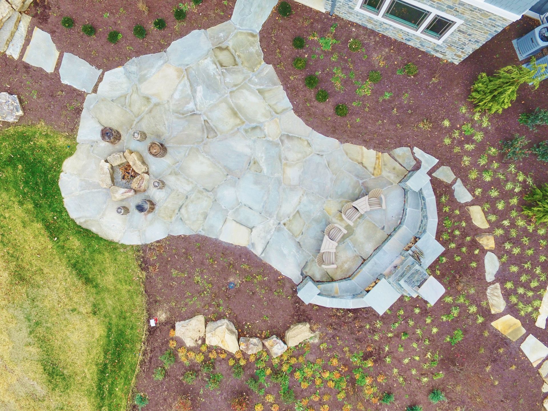 Aerial view of a backyard with a stone patio, curved steps, and surrounding mulch beds with plants