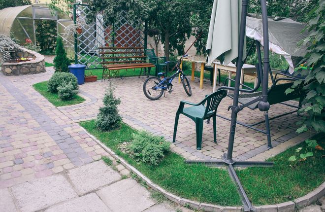 Garden patio with chairs, bicycle, and umbrella beside a paved path and small lawn