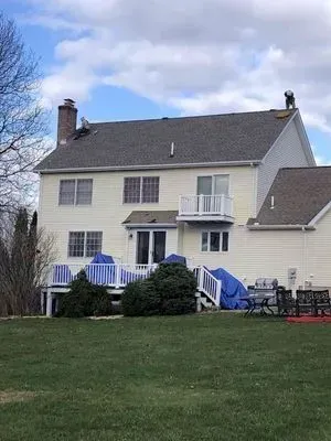 Back of a two-story beige house with a gray roof. A person is on the roof near the chimney.