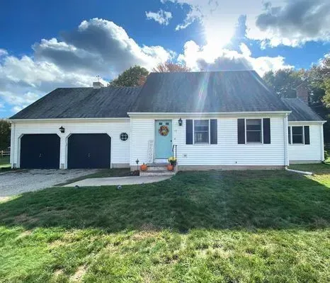 White ranch house with black garage doors, blue door, and green lawn under a sunny sky.