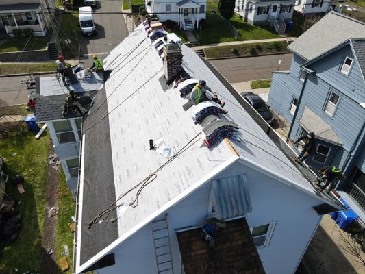 Roofers working on a residential house with safety gear, removing and replacing shingles, and a ladder for access.