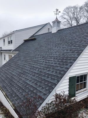 Gray asphalt shingle roof on a white house with a weathervane, against a cloudy sky.