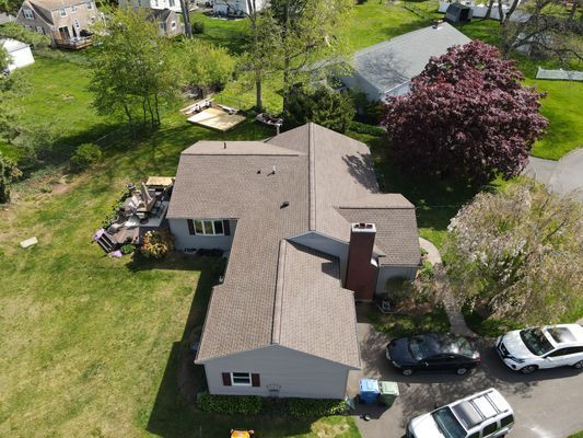 Aerial view of a gray house with a brown roof and a black car in the driveway. Green grass surrounds it.