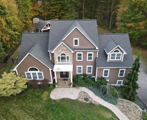 Brown two-story house with gray roof, stone accents, and manicured lawn.