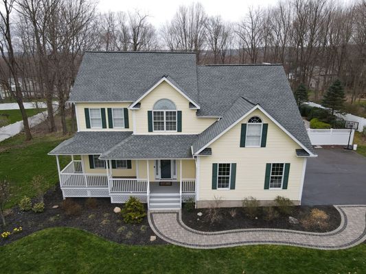 Yellow two-story house with green shutters and gray roof; pathway leads to the front entrance.