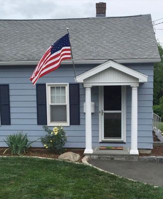 Blue house with American flag, white columns, black shutters, and a front yard.