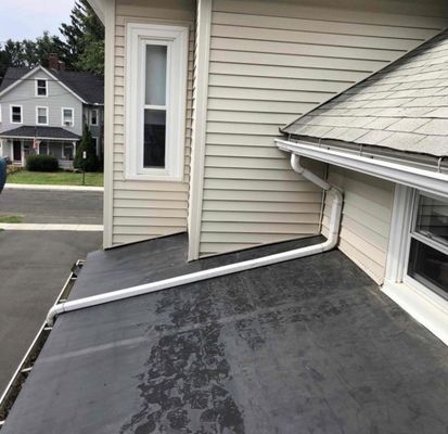 Black flat roof with white gutters and siding on a building. Another house in the background.