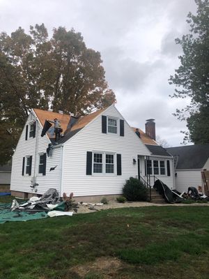House with roof partially removed, construction underway, surrounded by debris, overcast sky.
