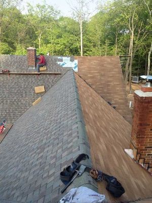 Roofers installing new shingles on a house roof. One worker on the roof near a chimney.