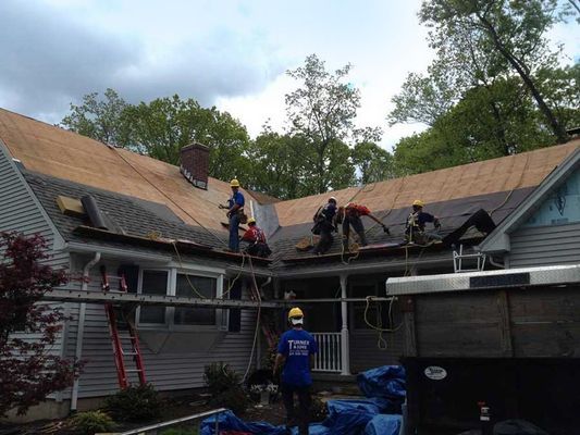 Roofing crew working on a house roof under a cloudy sky.