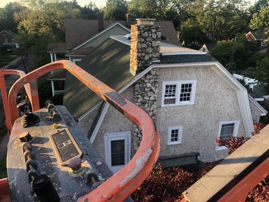 Cottage with stone chimney and light-colored siding, viewed from an aerial lift with an orange arm.