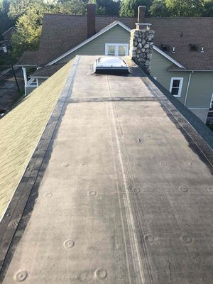 A flat, dark rooftop with a skylight, chimney, and adjacent pitched roof of a building.