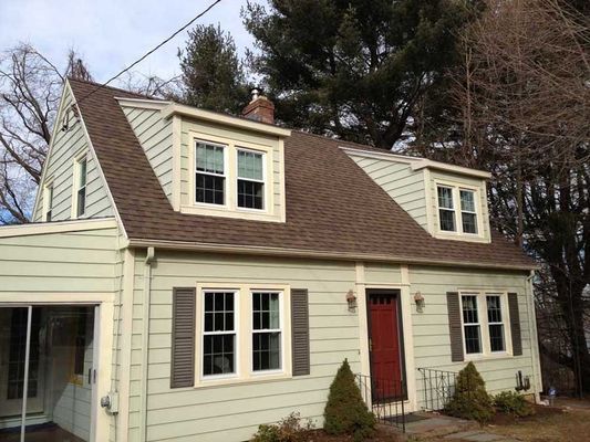 Light green house with brown roof, dormers, and red front door.