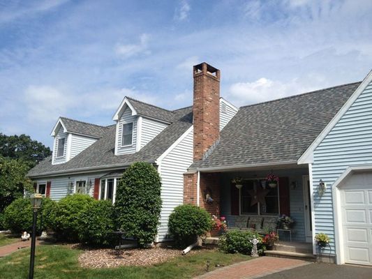 Blue house with gray roof, chimney, and dormers under a blue sky.