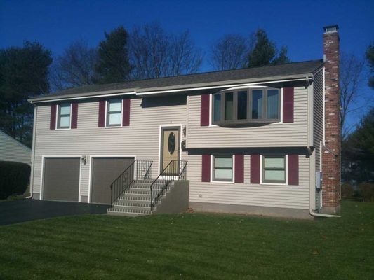 Tan two-story house with burgundy shutters, bay window, two-car garage, brick chimney, and green lawn.