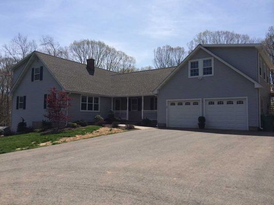 Light blue house with two-car garage, driveway, and front porch on a sunny day.