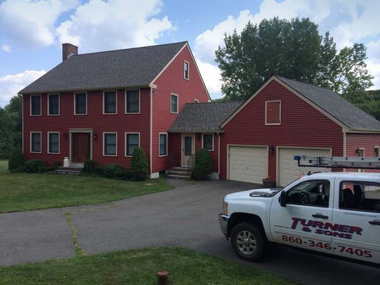 Red house with gray roof, driveway, and white work truck with the name 