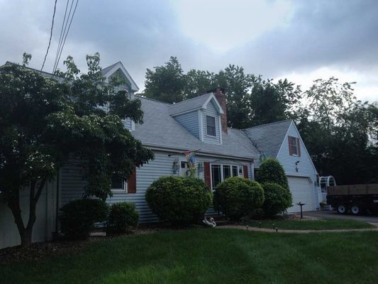 Blue house with gray roof, red shutters, and manicured green lawn under cloudy sky.