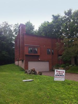 Brown house with garage, chimney, and sign for Turner & Sons on a grassy lawn.