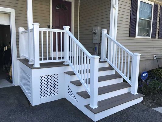 White railing and steps leading up to a house entrance with a burgundy door.