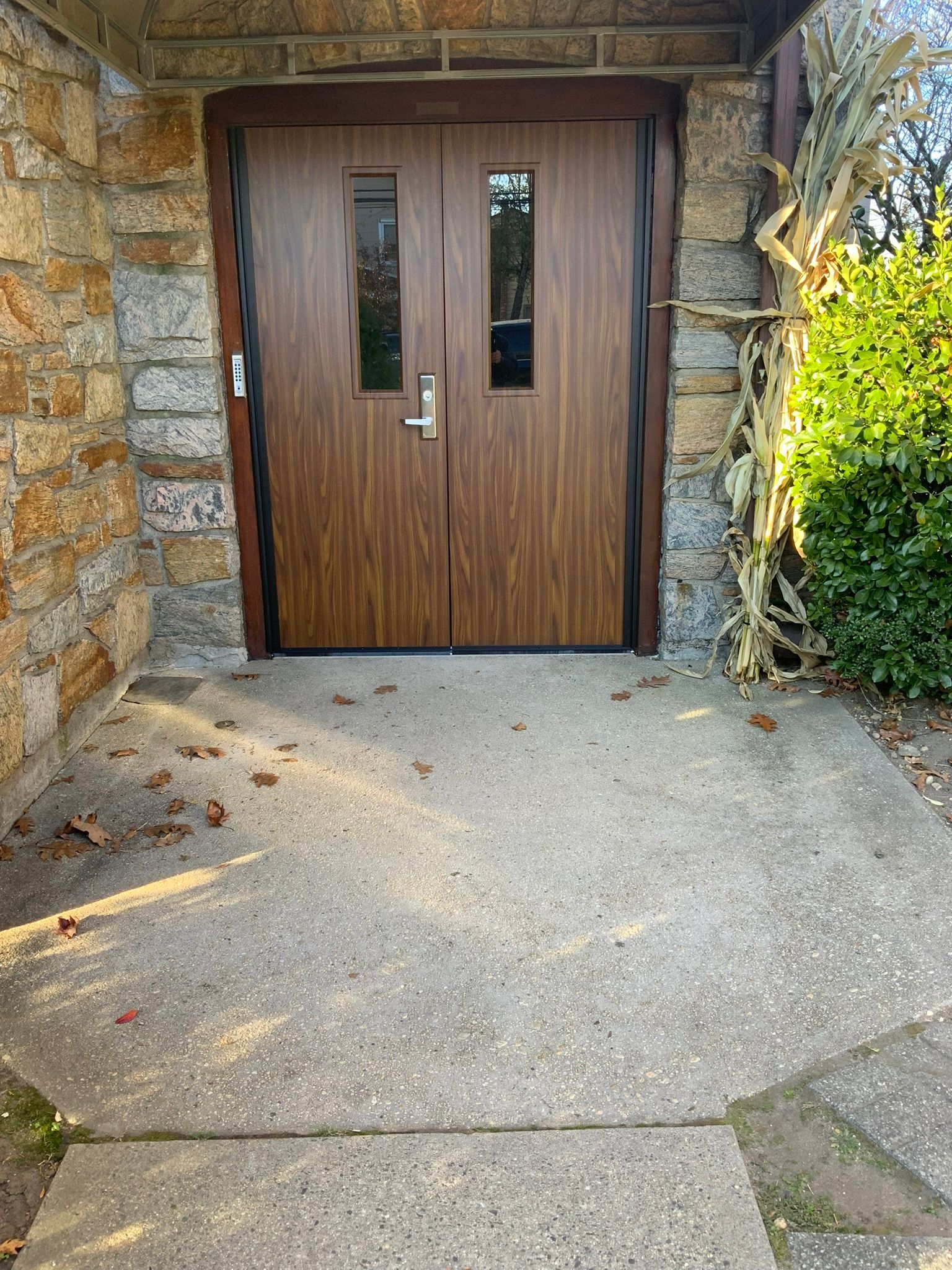Brown double doors with rectangular windows set in a stone doorway. Concrete walkway in front.