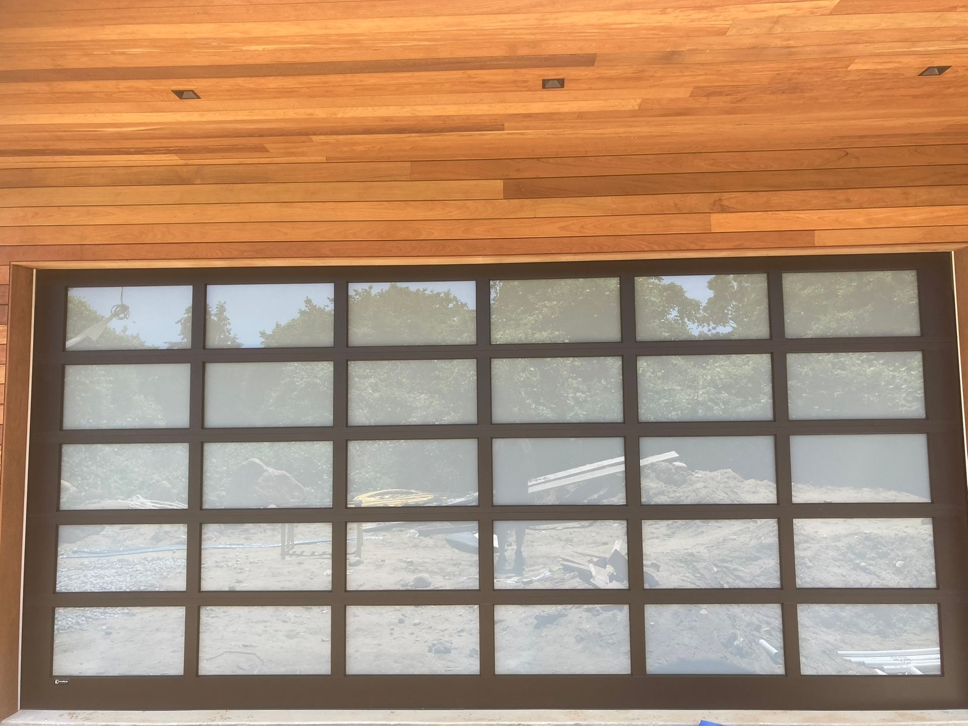 A modern garage door with square glass panels, framed in dark metal, set against a wooden facade.