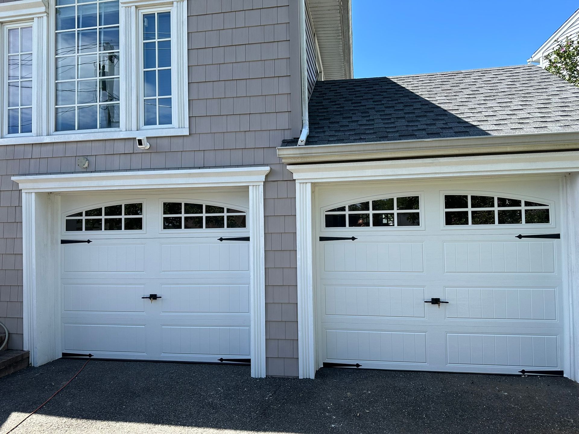 Two white garage doors with arched windows, on a gray shingled house.