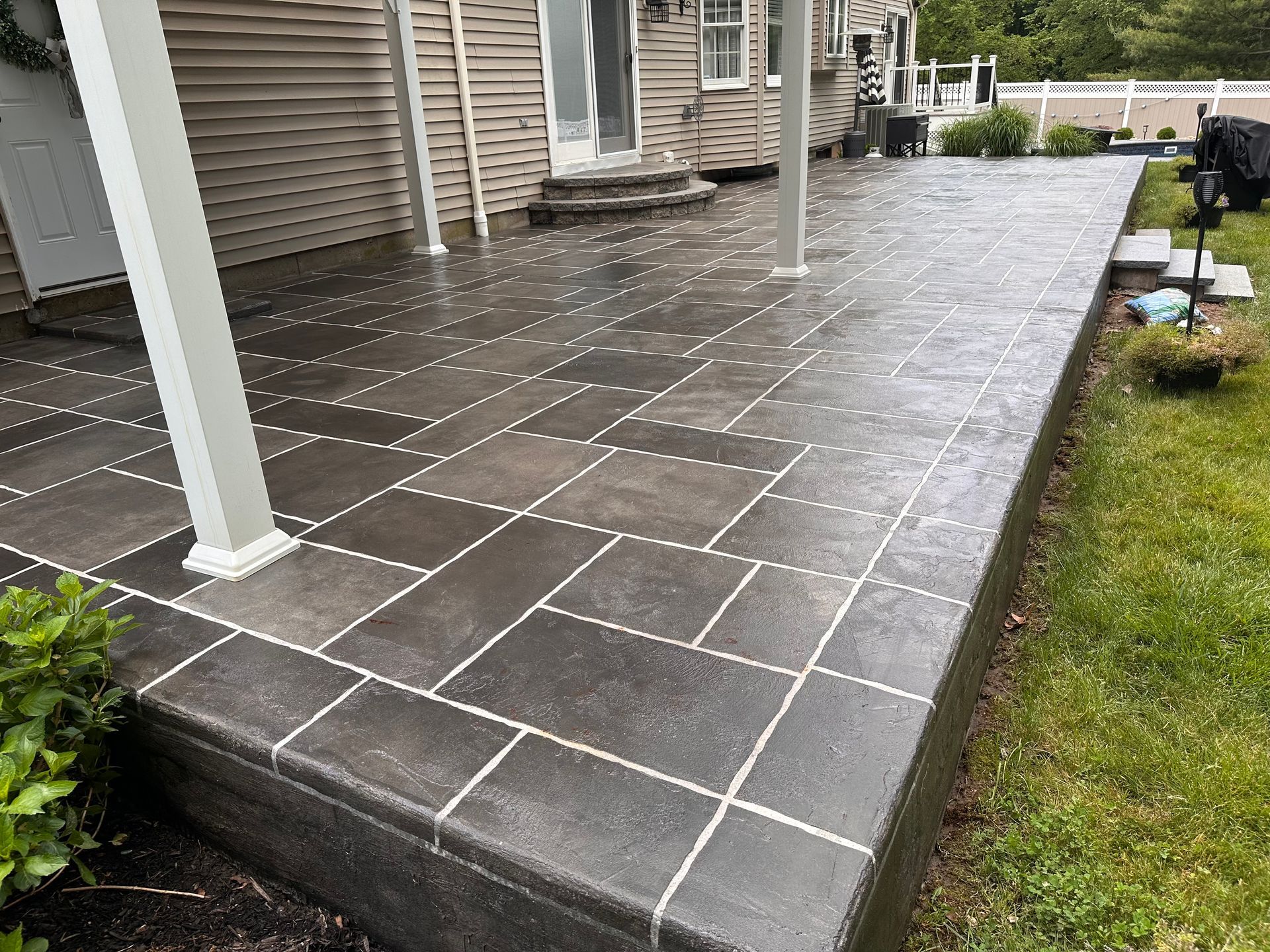 A concrete patio with a white fence and a house in the background.